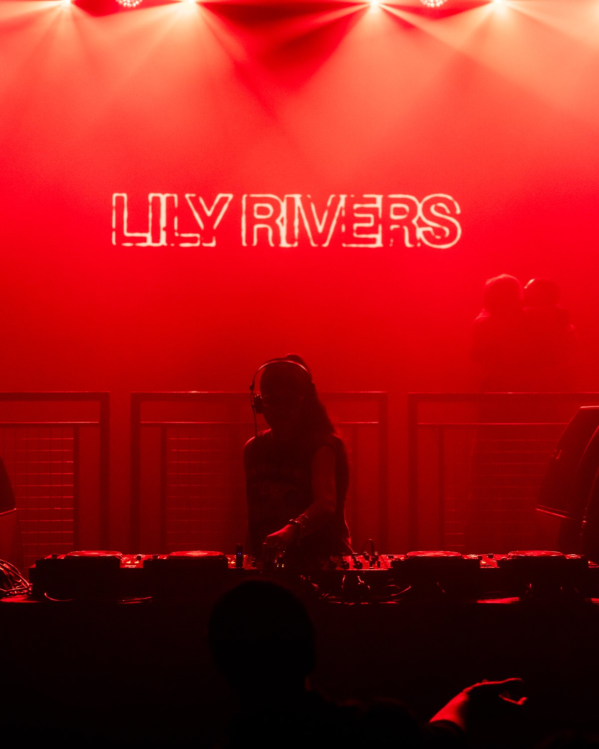 Lily Rivers DJing at KOKO London, her name in neon above the decks