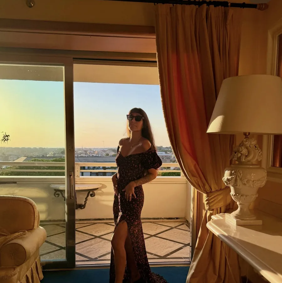 Lily Rivers in an evening gown by a hotel window at sunset